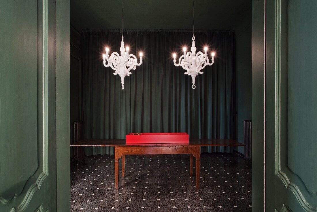 Modern white chandeliers in dark green room with wall panelling and terazzo floor