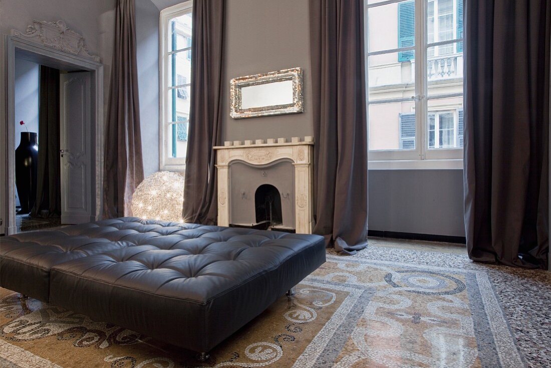 Black leather ottoman on terrazzo floor in front of open fireplace in elegant old building