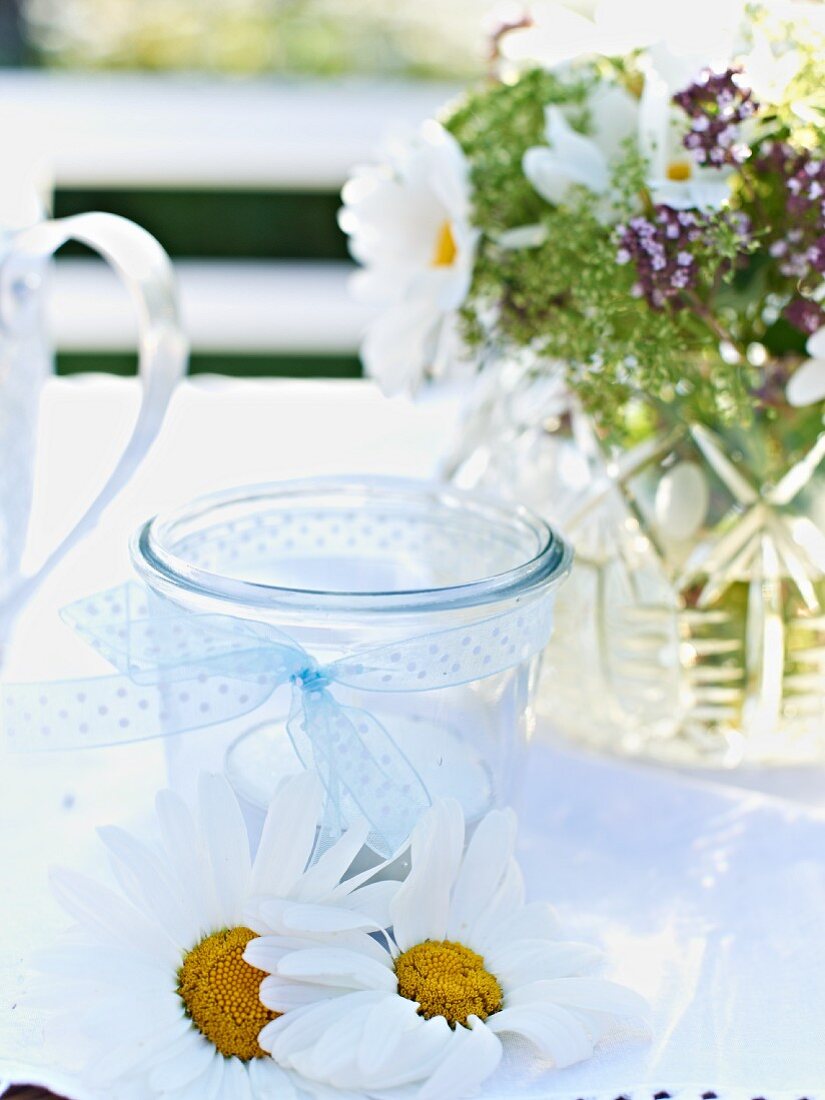 Teelicht, Margeritenblüten und Blumenstrauss als Deko auf Gartentisch