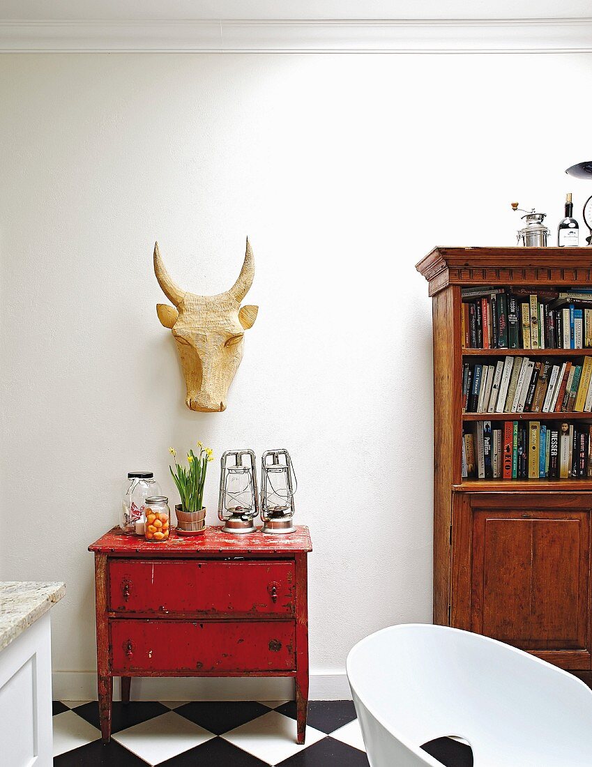 Carved ox head above old, red chest of drawers next to bookcase