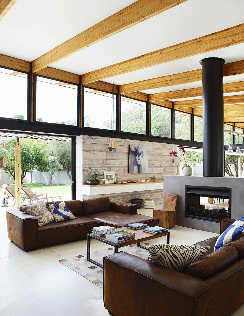 Brown leather sofas and coffee table in front of fireplace in open-plan interior with transom windows and wood-beamed ceiling