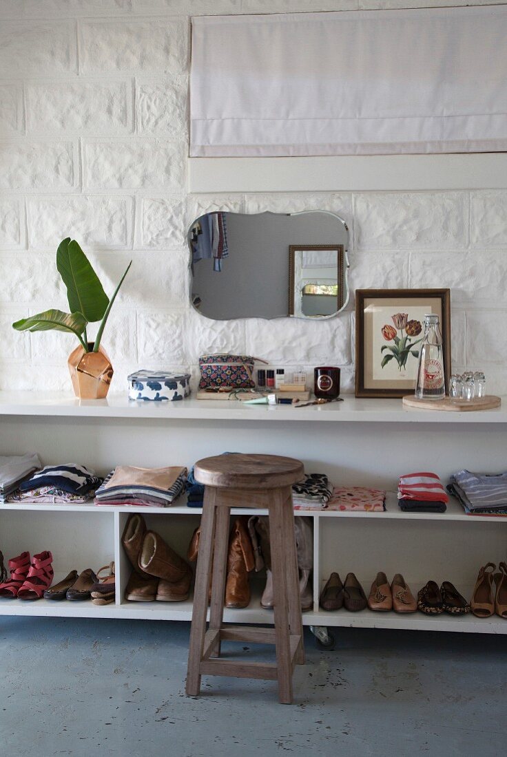 Wooden stool in front of clothing and children's shoes on shelves of white, open-fronted sideboard