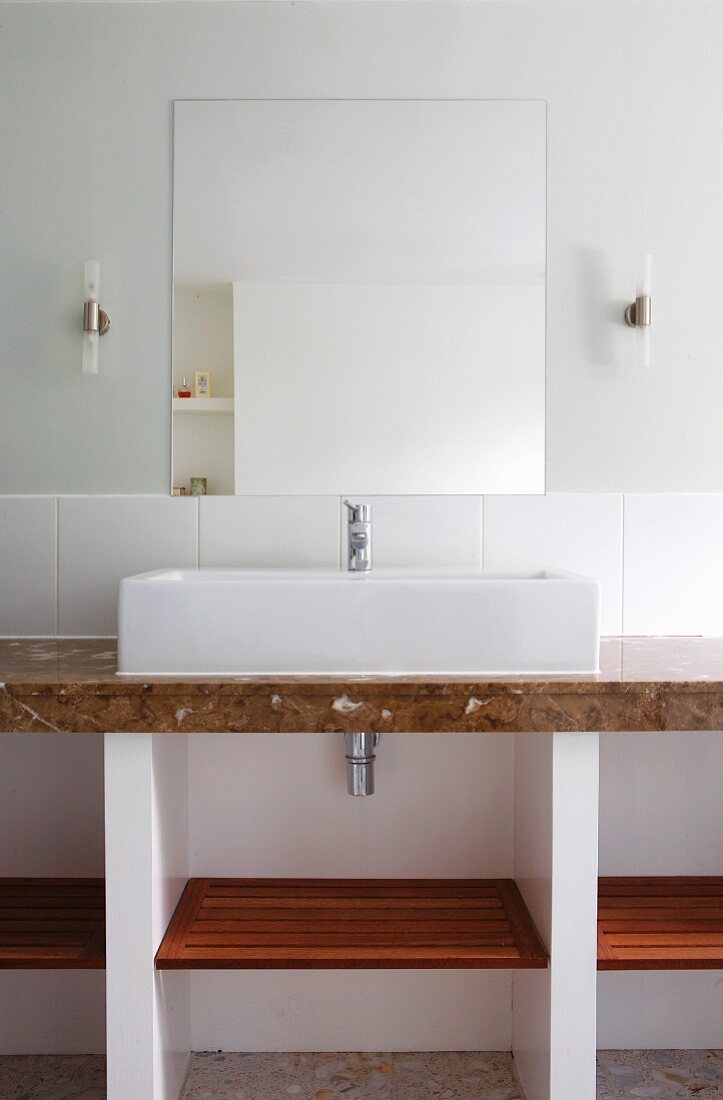 Washstand with countertop sink on marble counter against wall with half-height white tiles below mirror flanked by sconce lamps