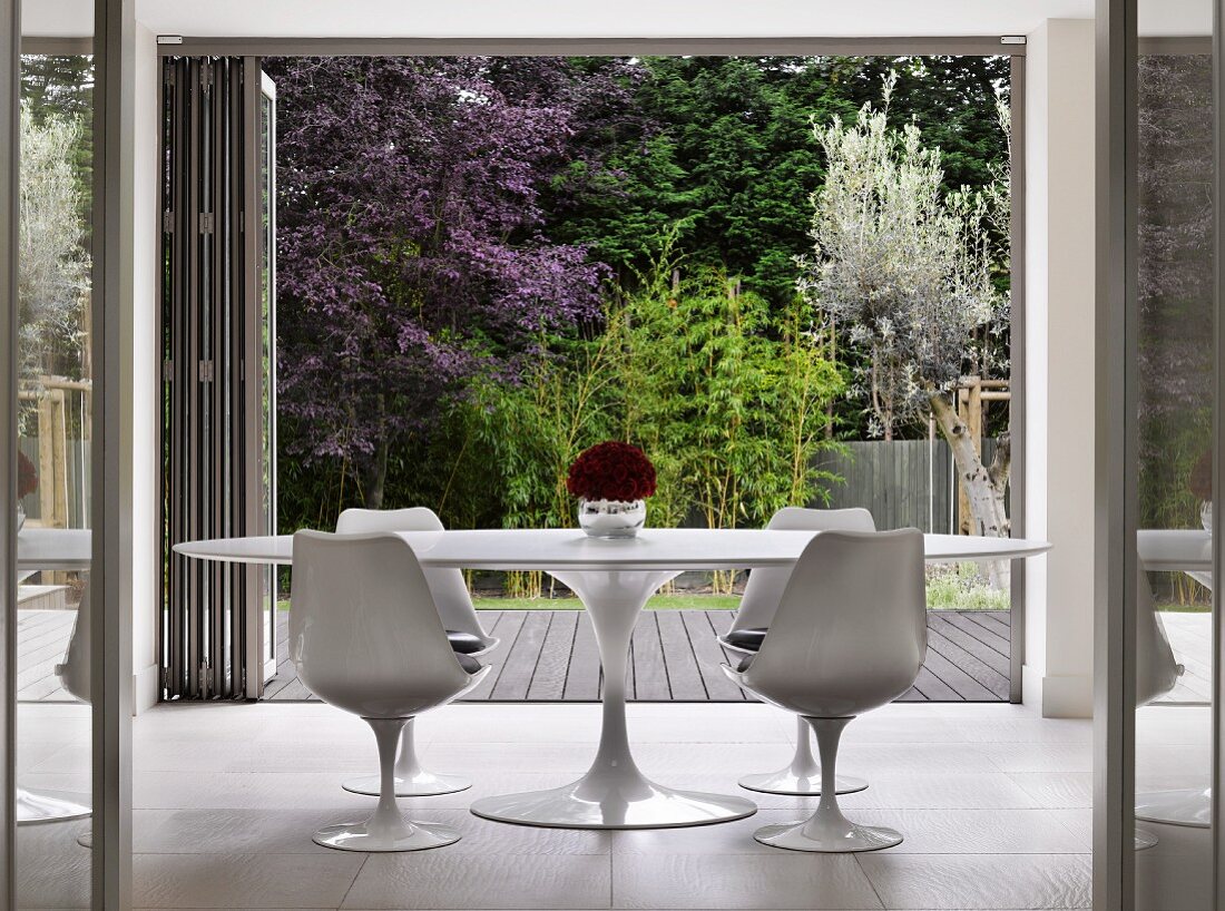 White, classic Tulip Table and matching chairs in front of open folding chairs with view into garden