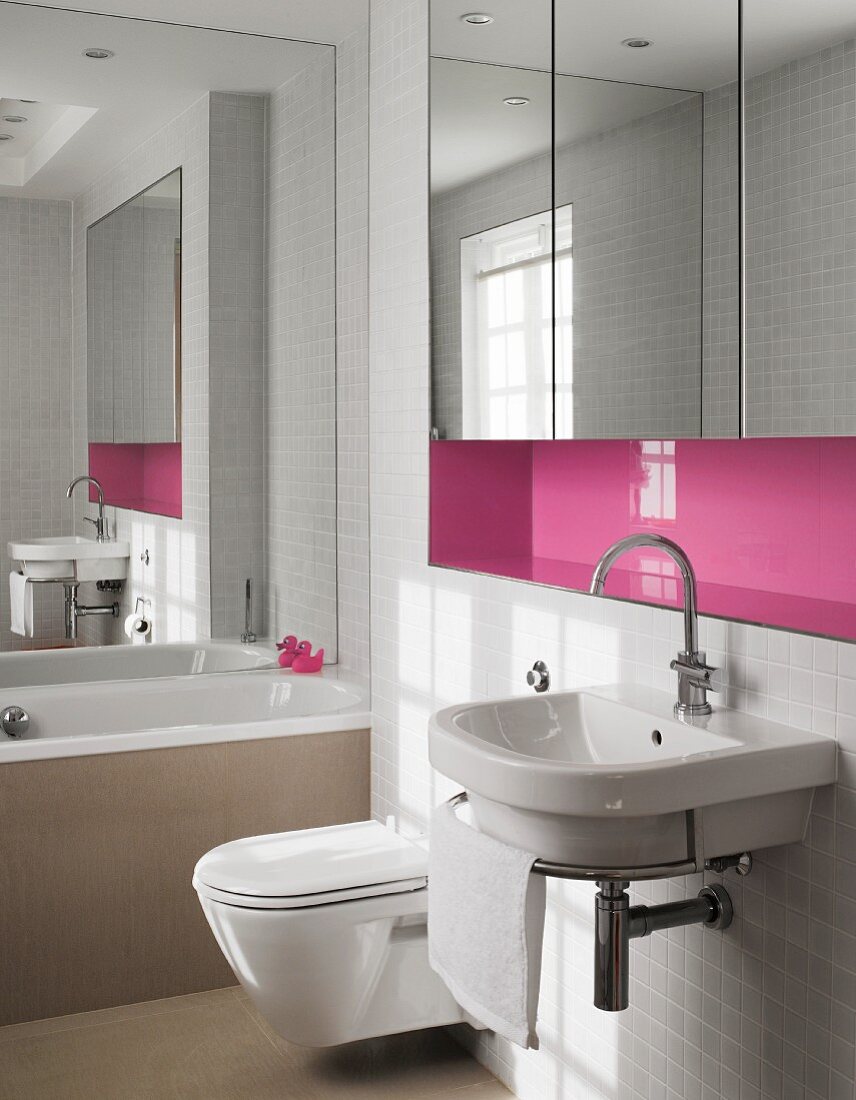 Sink with towel rail below pink niche with fitted, mirrored cabinets in bathroom