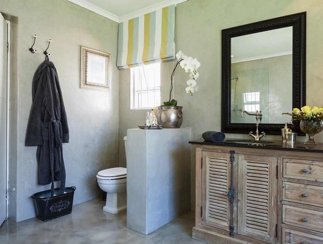 WC mit brüstungshoher Trennwand neben Vintage Waschtisch aus Mangoholz und schwarz gerahmtem Spiegel