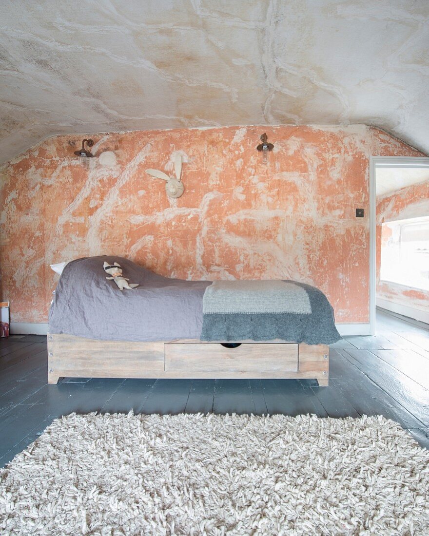 Soft toy on child's bed with drawers below in purist, renovated attic room with patinated walls and ceiling