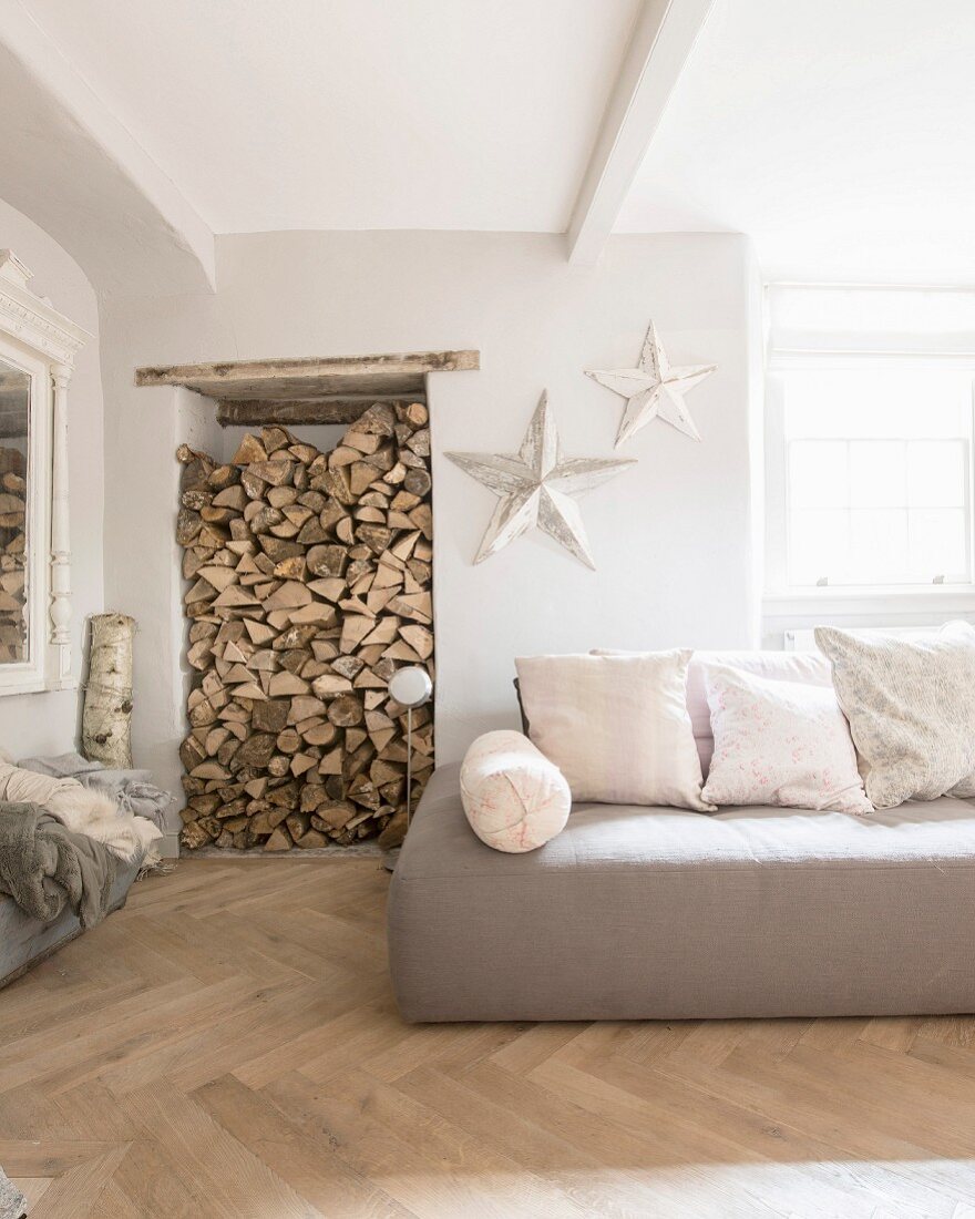 Wandnische für Brennholz neben Sofa mit Kissen, weiße Dekosterne mit Patina an der Wand