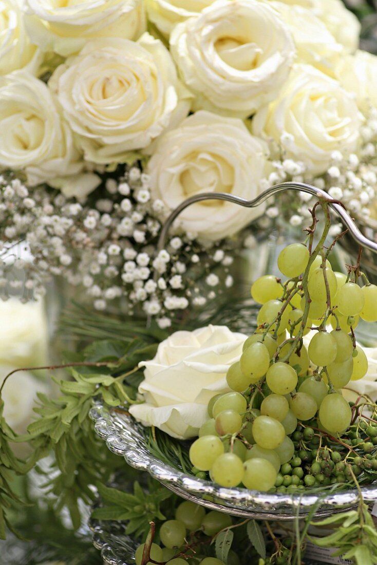 Bouquet of white roses and gypsophila behind white grapes on cake stand