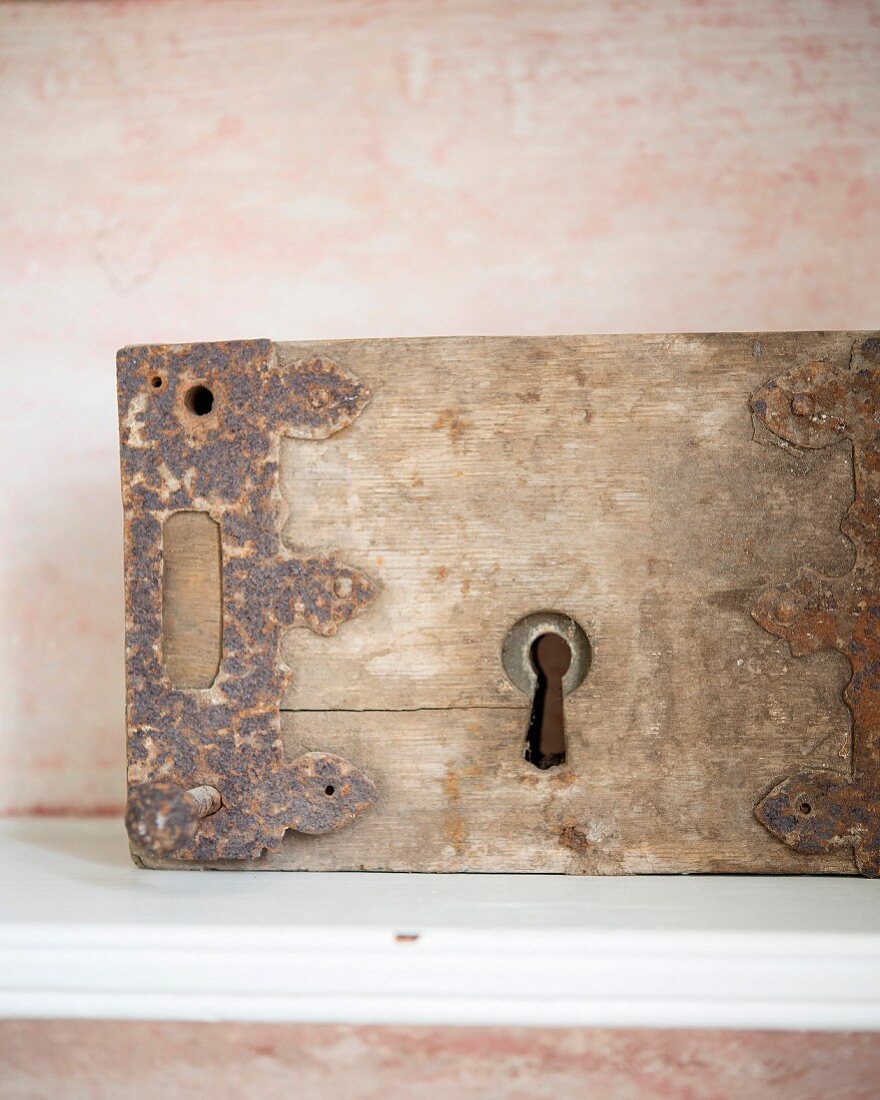 Rostiger Beschlag an Vintage-Holzstück mit Schlüsselloch vor zartrosa patiniertem Hintergrund
