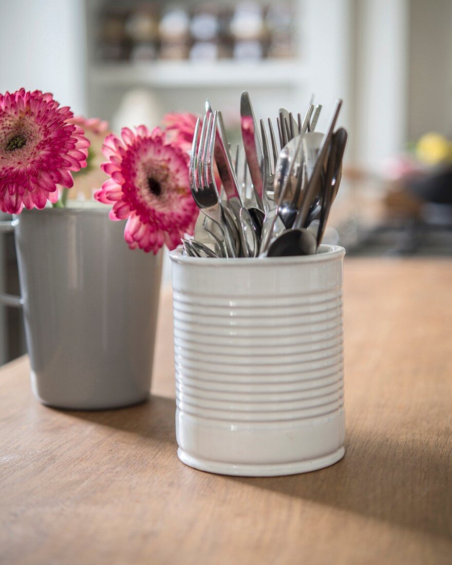 Besteck in weißem Keramikbecher und Blumen in grauer Tasse auf Küchenarbeitsplatte