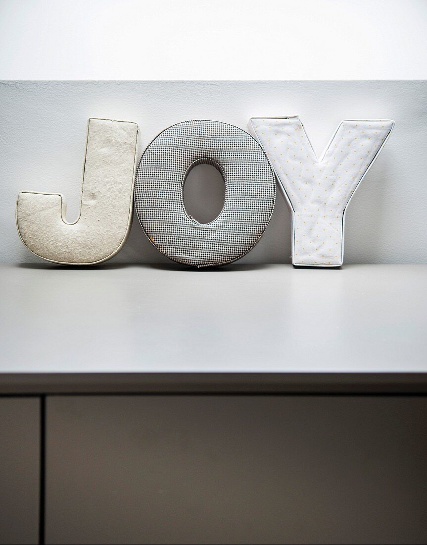Aufgestellte Dekobuchstaben 'JOY' aus Stoff auf hellgrauer Ablage