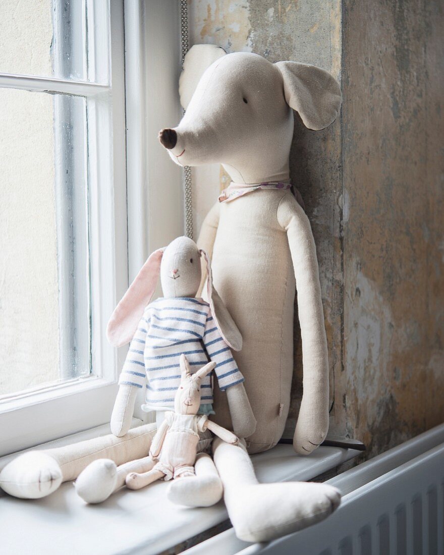 Various soft toys sitting on window sill leant against wall with vintage patina