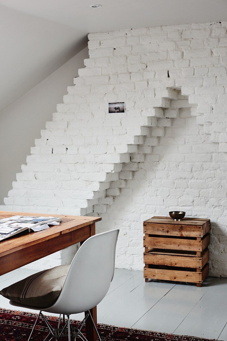 Wooden table and classic chair in front of rustic console table made from wooden crates in whitewashed brick niche