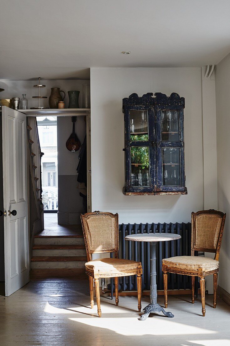 Zwei antike Stühle um Bistrotisch, Vitrinenschränkchen über Heizkörper, seitlich offene Tür und Blick in Hauseingang