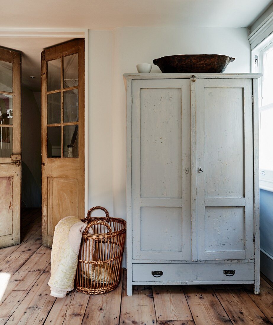 Simple wooden cupboard and basket in corner of room next to double doors