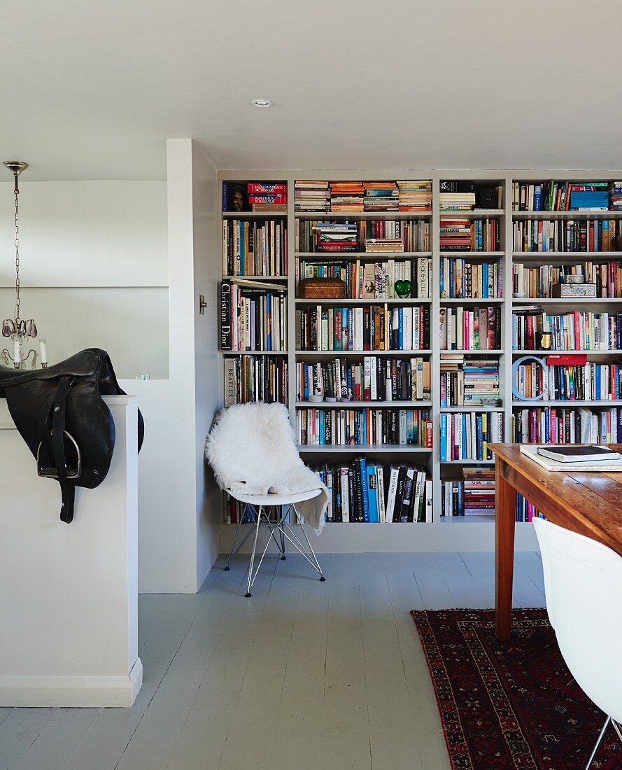 Klassiker Schalenstuhl mit weißem Tierfell vor Bücherwand in schlichtem Ambiente