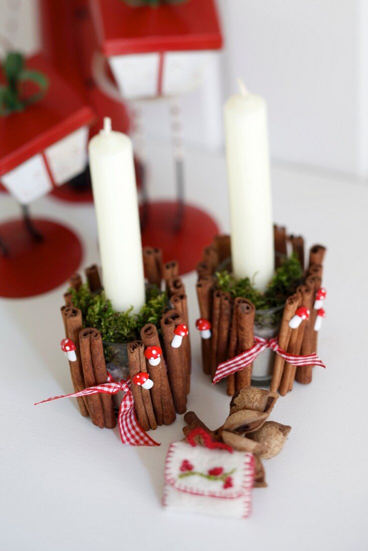Festive, glass candle holders decorated with cinnamon sticks, ornamental toadstools and moss