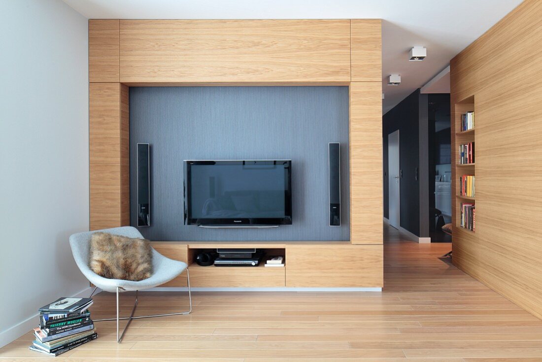 Designer armchair in front of wooden living room wall with flatscreen TV and speakers in niche in open-plan interior