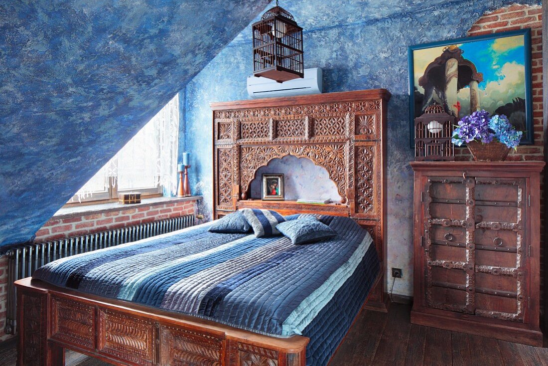 Bed with carved wooden frame and Oriental-style headboard in attic room with mottled blue walls