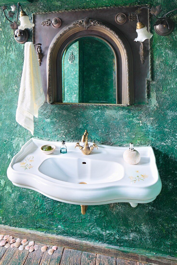 Curved sink with vintage brass taps and mirror with Oriental-style frame on green wall