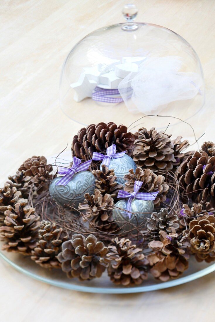 Weihnachtlicher Tischschmuck aus Kiefernzapfen & Dekoherzen auf Glasteller mit Glasglocke
