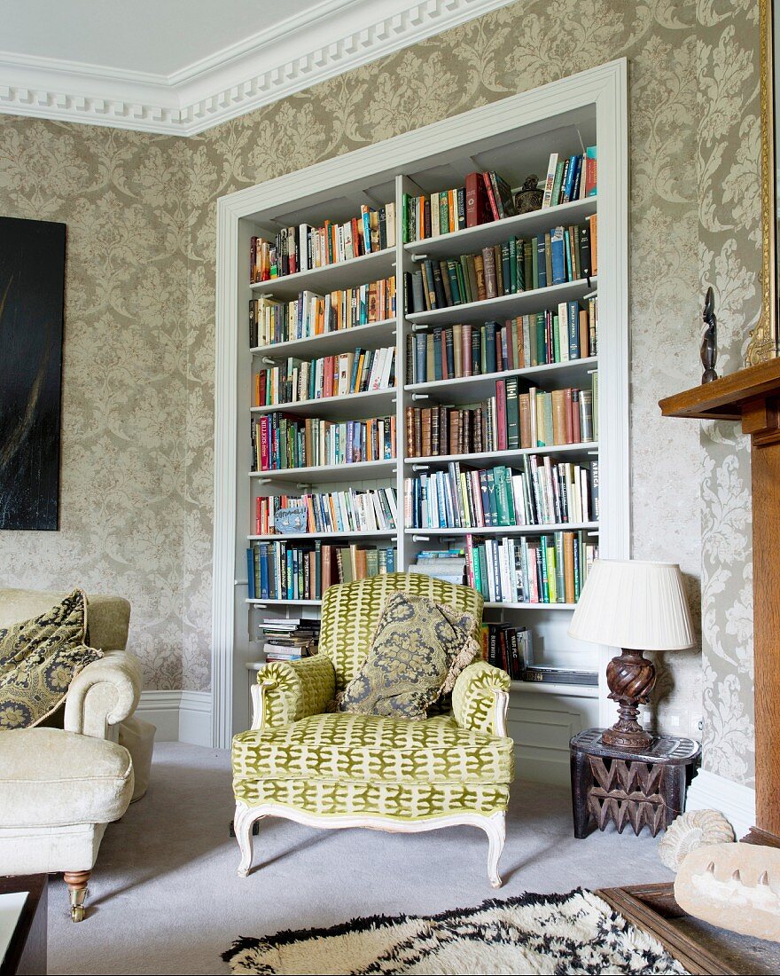 Rokoko Sessel mit gemustertem Bezug vor Bücherschrank in Wandnische in traditioneller Wohnzimmerecke mit Ornamenttapete
