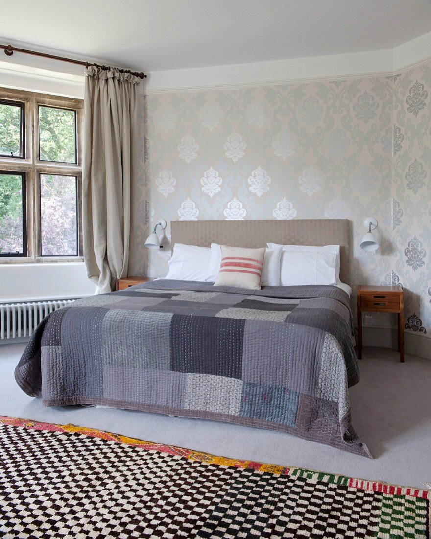 Checked rug in front of double bed with patchwork blanket in various shades of grey in traditional bedroom