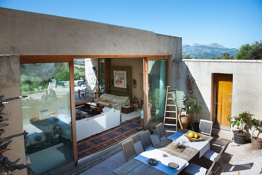 Terrasse eines mediterranen Bungalows mit großem Esstisch aus Holz und Blick in den Wohnraum