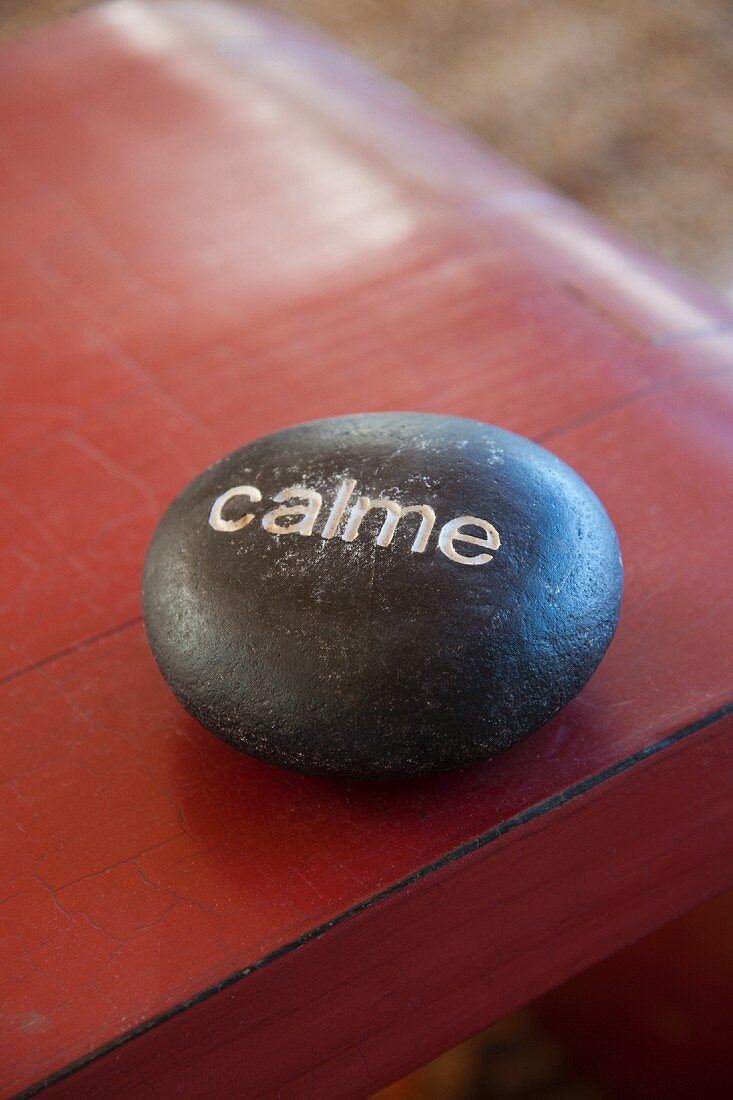 Mit dem Wort 'calme' beschrifteter schwarzer Stein auf einem rot lackierten Tisch
