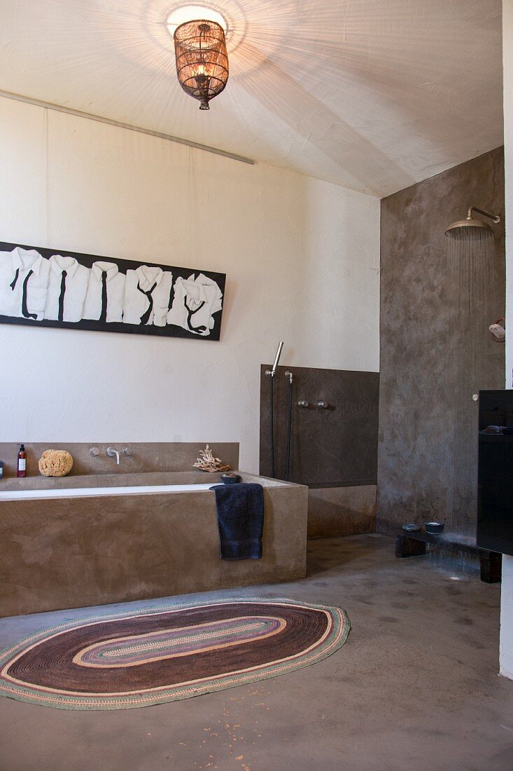 Badezimmer im Ethnostil mit grau verputzten Wänden, gemauerter Badewanne und offener Dusche