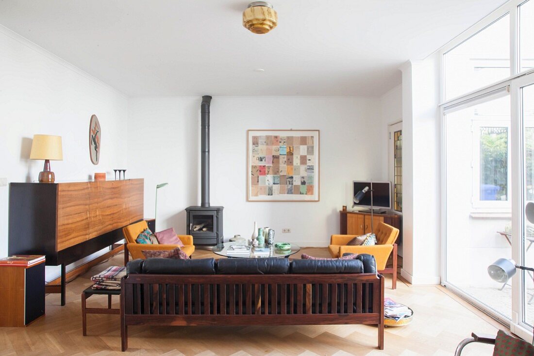 Sitzbank mit Holzgestell und schwarze Lederpolster, seitlich Sideboard in schlichtem Wohnzimmer mit Kaminofen