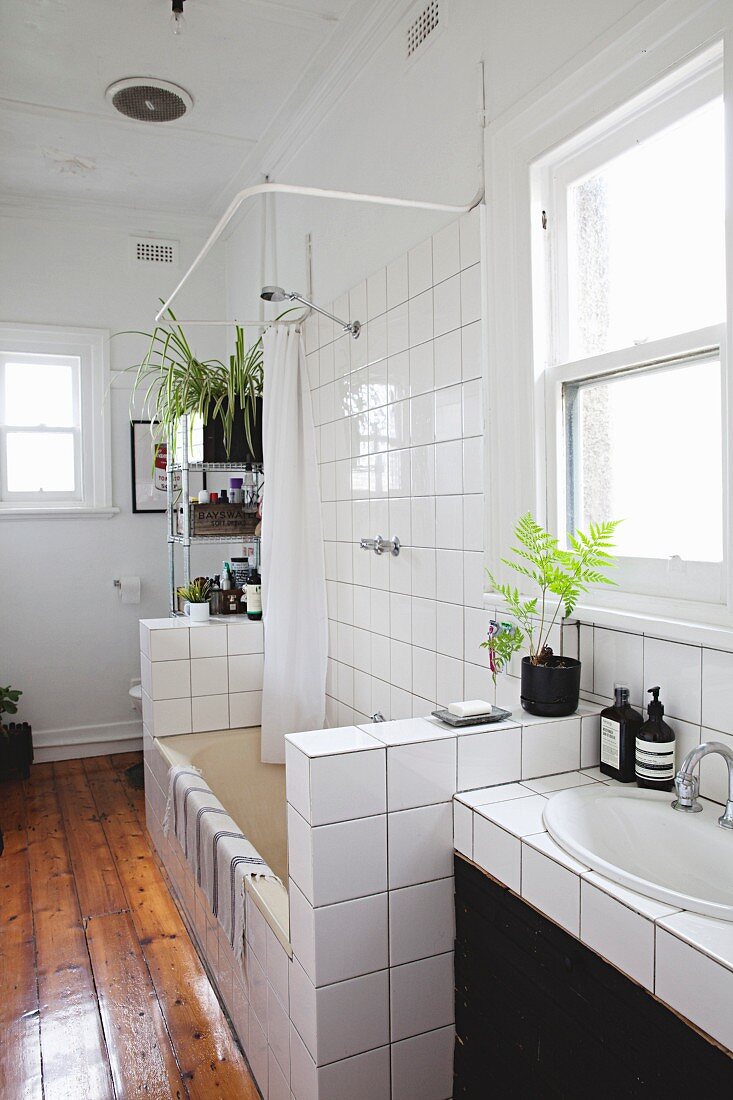Waschtisch und Wanne mit halbhohen, gefliesten Trennwänden und lackierter Dielenboden in Altbau Badezimmer