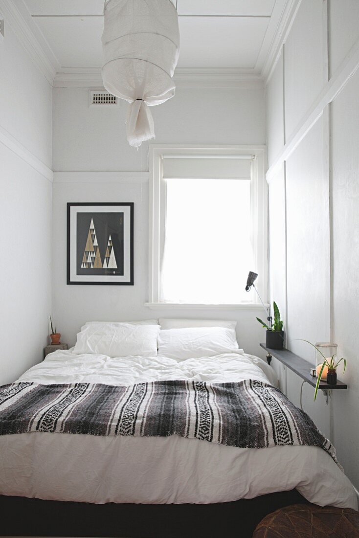 Doppelbett vor Fenster in schmalem Schlafzimmer mit schlichter Wand- und Deckenvertäfelung in Weiß