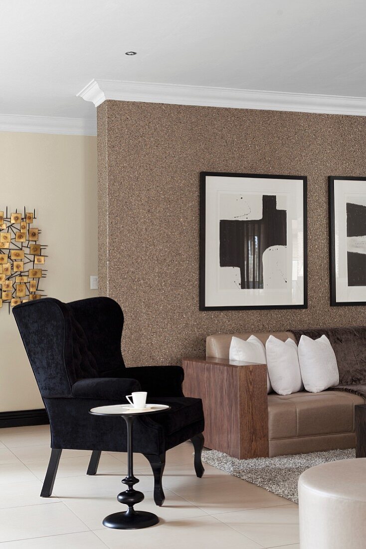 Schwarzer Ohrensessel und Beistelltisch neben teilweise sichtbarem Sofa vor Wand mit brauner Strukturtapete