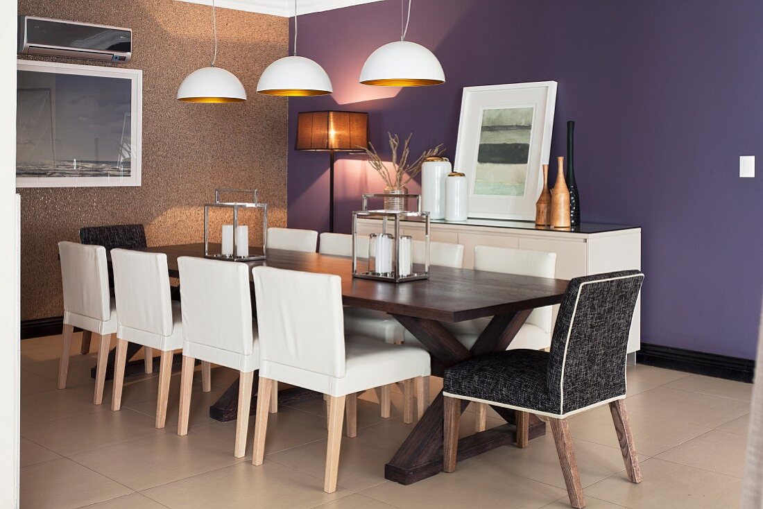 White leather chairs at long, dark-wood table below pendant lamps with white and gold lampshades; purple-painted accent wall in background