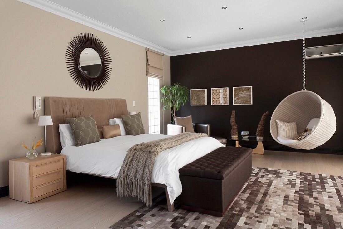 Elegantes Schlafzimmer in Brauntönen - gepolsterte Truhe vor Doppelbett und Hängeschaukel