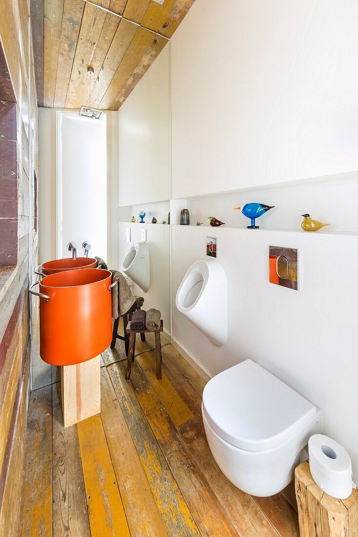 Modernes Bad mit WC und Urinalbecken, im Hintergrund Designer-Waschbecken aus orangefarbenem Kochtopf