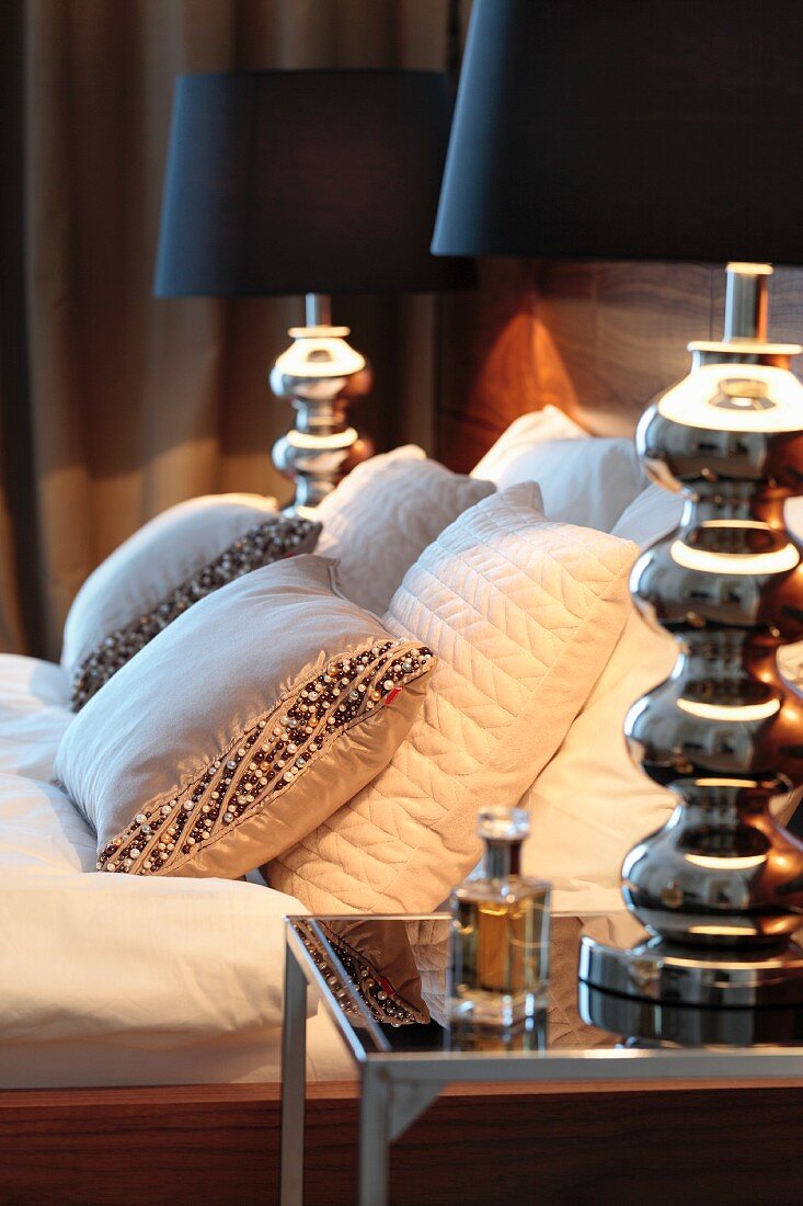 Designer lamp on bedside table next to bed with bead-embroidered scatter cushions