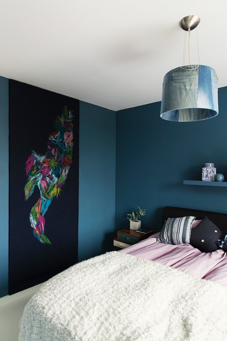 Bett mit weisser Tagesdecke und Wandbehang an blau getönter Wand in modernem Schlafzimmer