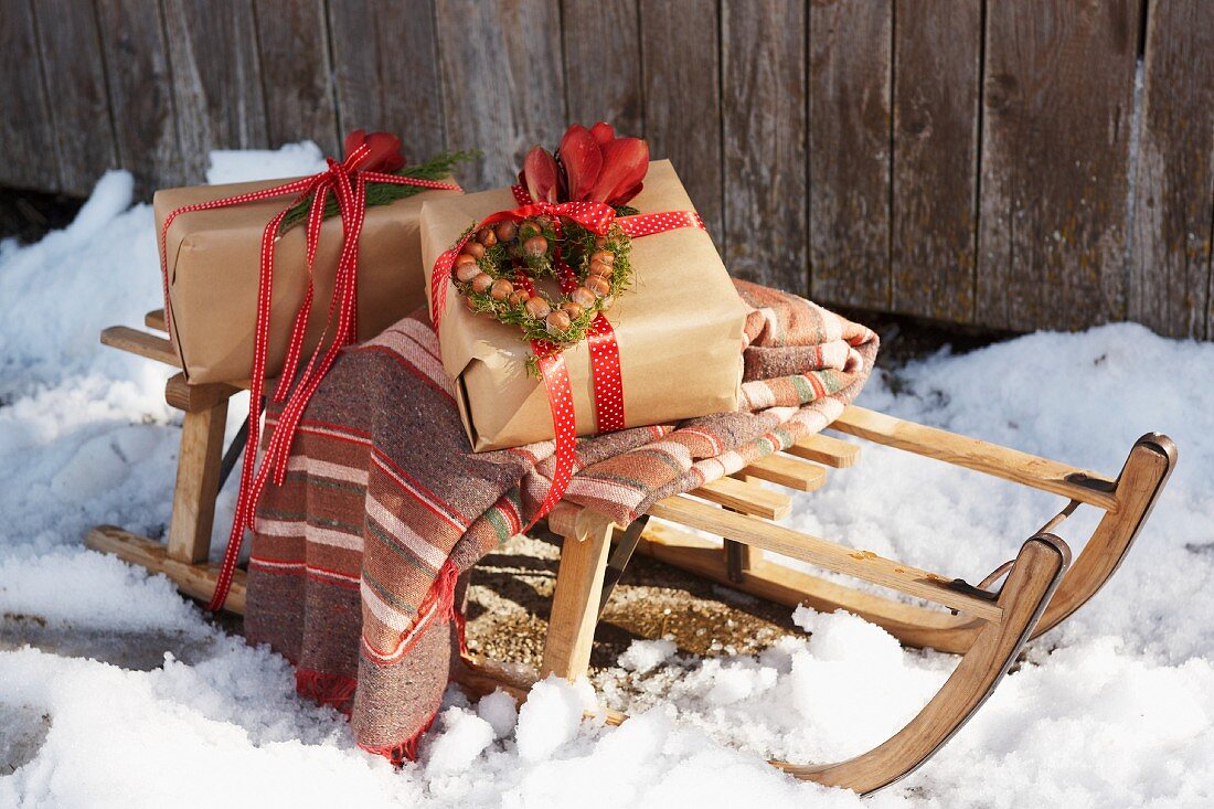 Zwei in Packpapier verpackte Geschenke und gestreifte Decke auf Holzschlitten im Schnee