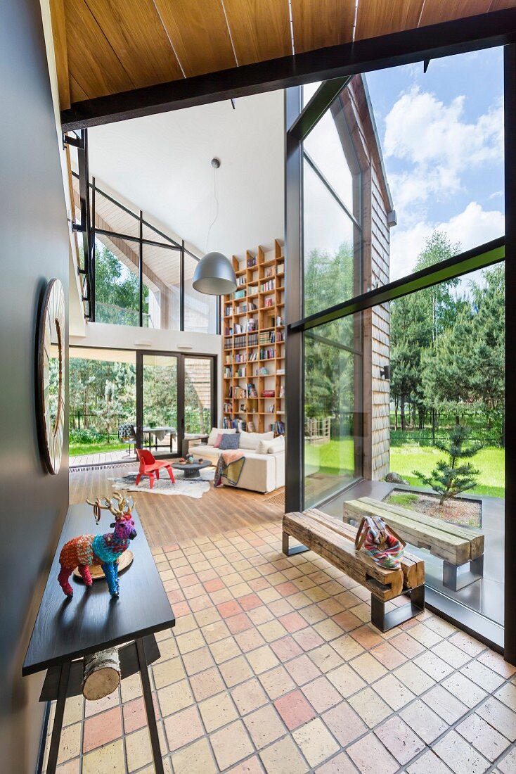 Spacious interior with tiled floor and black console table opposite glass facade with view into sunny garden