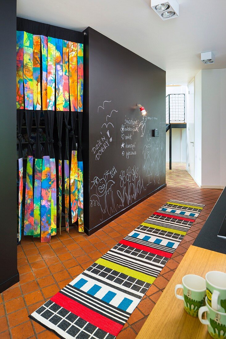 Brightly patterned rug on tiled floor and chalk drawings on wall painted with chalkboard paint