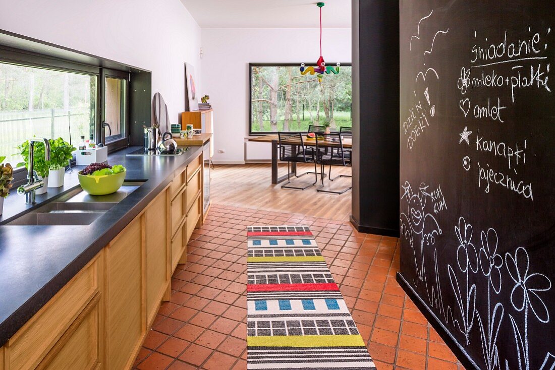 Offene Küche mit buntem Teppichläufer auf Fliesenboden, schwarze Wand mit Tafellack