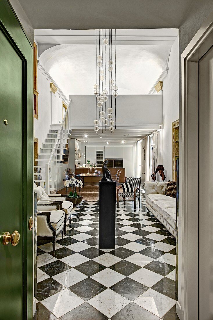 Blick durch offene Tür in elegantes Foyer mit Schachbrettmusterboden, oberhalb moderne Pendelleuchte