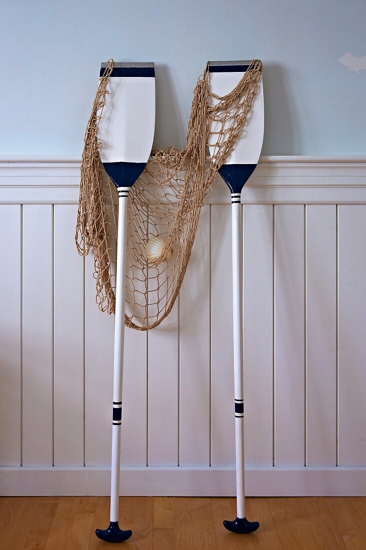 Maritime arrangement of white and blue paddles and fishing net leaning against white wainscoting