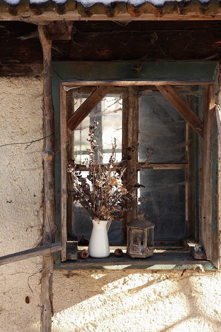 Trockenblumenstrauss auf Fenstersims vor ländlichem Holzfenster