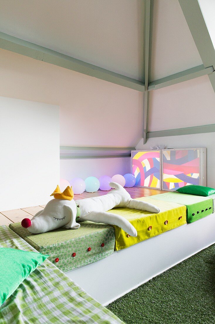 Colourful floor cushions and soft toys in seating area in child's attic bedroom