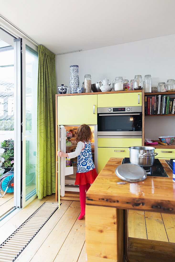 Gelbe Küchenzeile neben Terrassenschiebetür, Kind am Kühlschrank