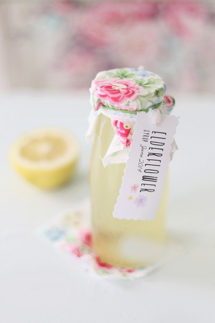 Bottled of home-made elderflower syrup trimmed with lovingly decorated label and rose-patterned fabric
